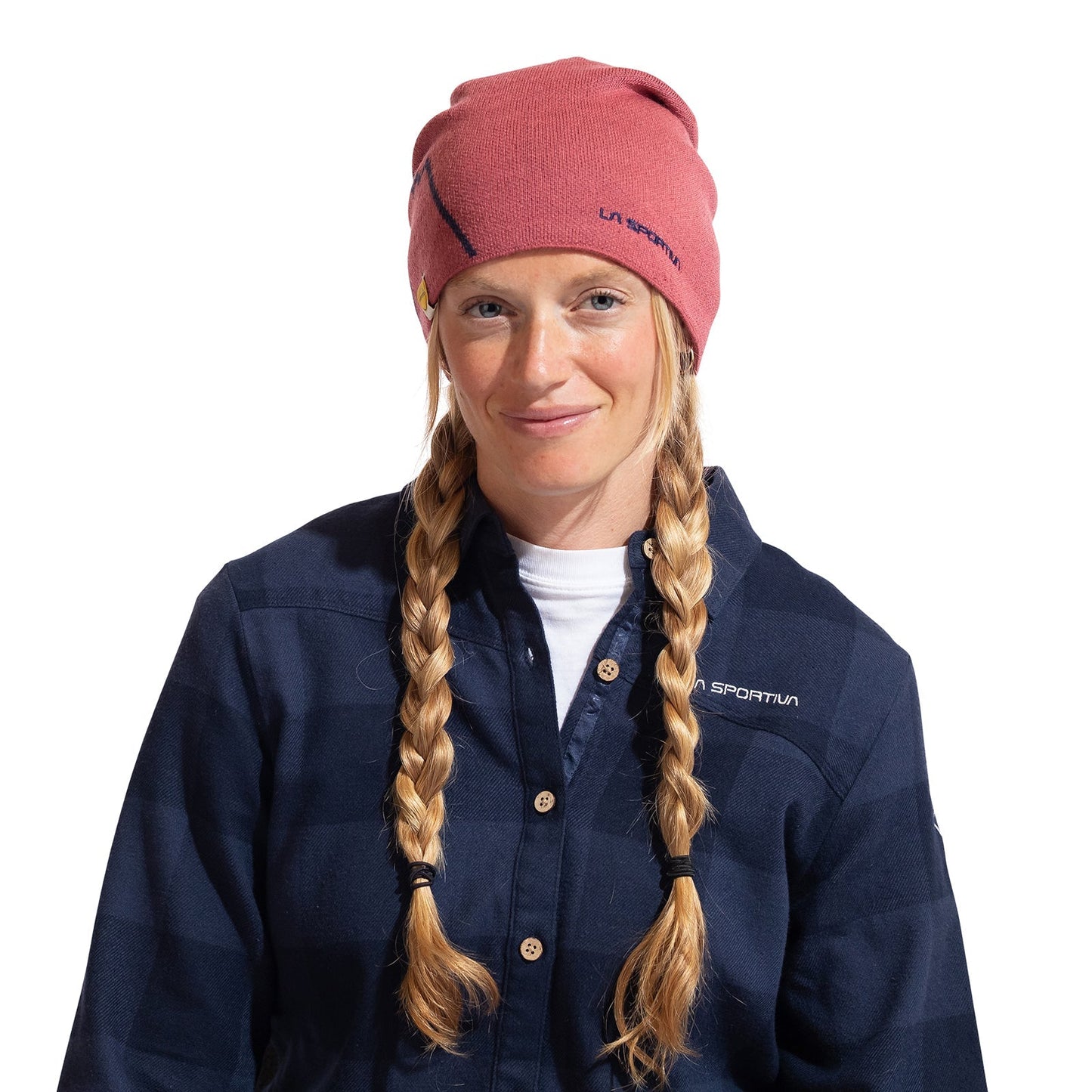 A woman with long blonde braids wears the La Sportiva Woolly Beanie and a navy blue plaid shirt, smiling softly at the camera against a plain white background, ready for cold weather.