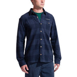 A man wears the La Sportiva Rambler Flannel Shirt Men's, a navy blue plaid cotton-polyester blend with a collar, chest pocket, light buttons, and the LA SPORTIVA logo, standing against a white background.