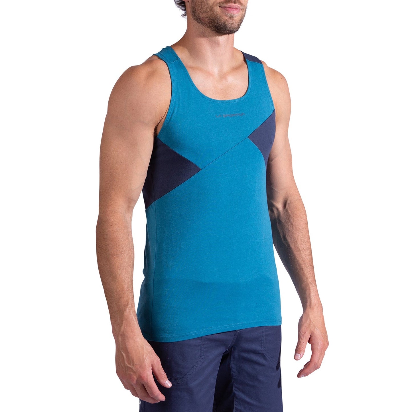 A man wearing the La Sportiva Dude Tank Men's—a sleeveless teal athletic top with angled navy panels—and dark blue shorts stands against a white background.