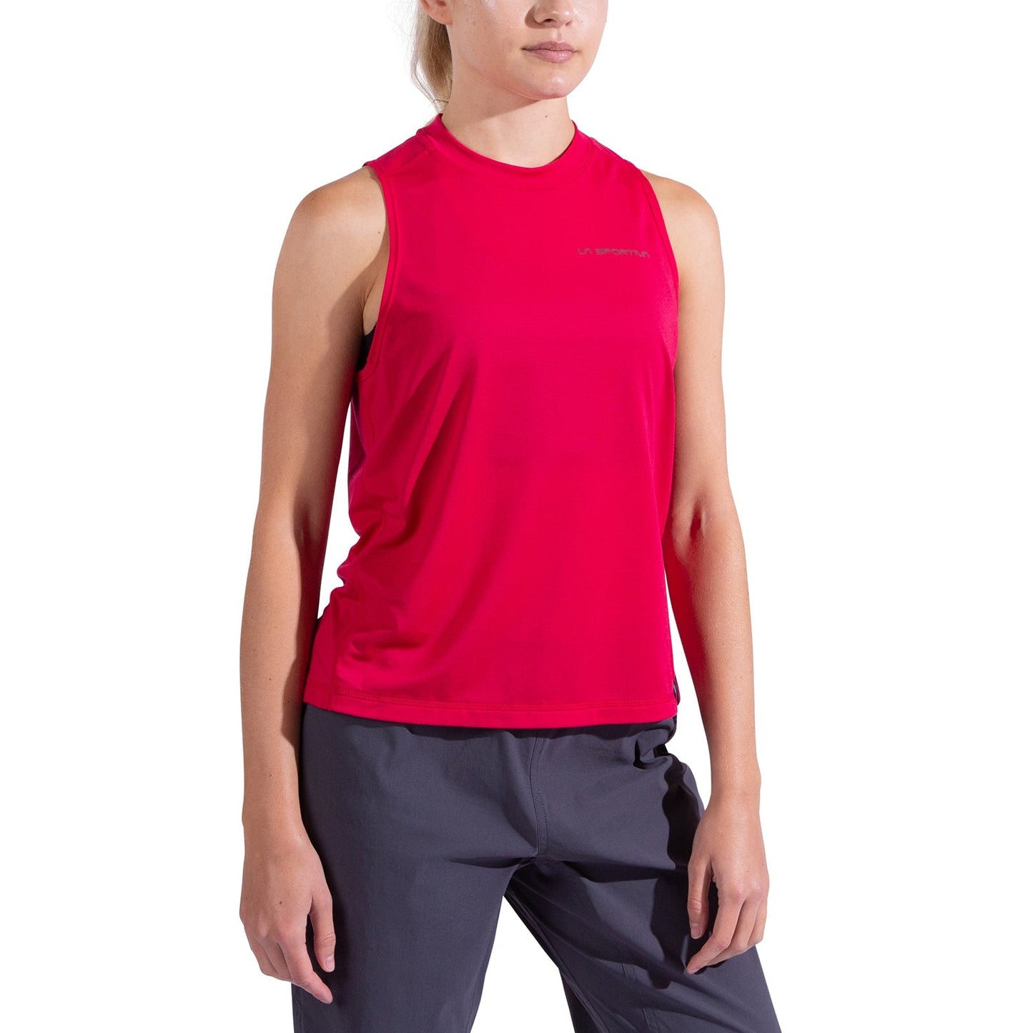 A woman models the La Sportiva Just Right Tank Women's—a sleeveless, bright pink moisture-wicking top—paired with dark gray pants against a plain white background. Her face is partially out of frame and her arms rest at her sides.