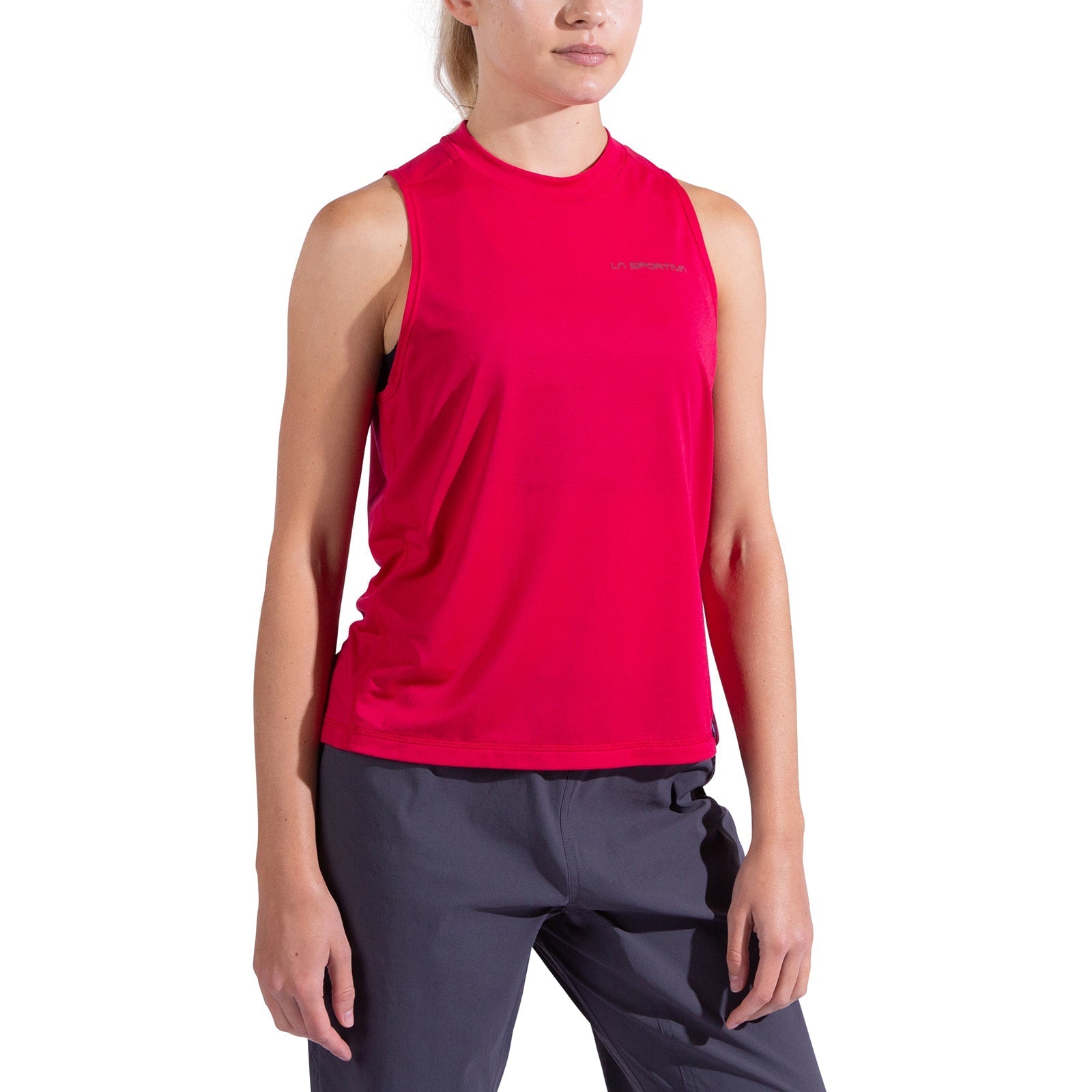 A woman models the La Sportiva Just Right Tank Women's—a sleeveless, bright pink moisture-wicking top—paired with dark gray pants against a plain white background. Her face is partially out of frame and her arms rest at her sides.