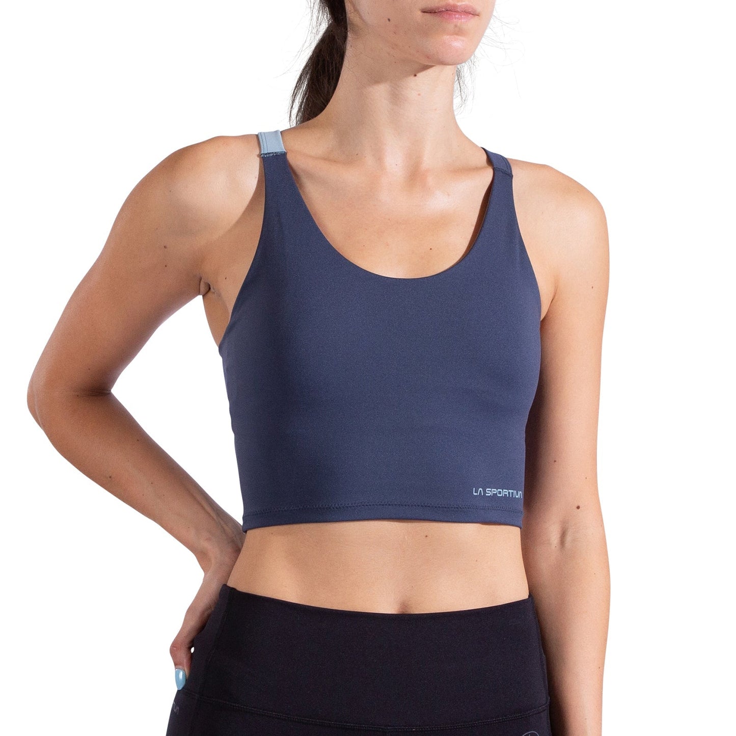 A woman stands with one hand on her hip against a white background, wearing the La Sportiva Cosmosis Bra Tank Women's in navy blue and black leggings. The crop top features a small La Sportiva logo near the hem.