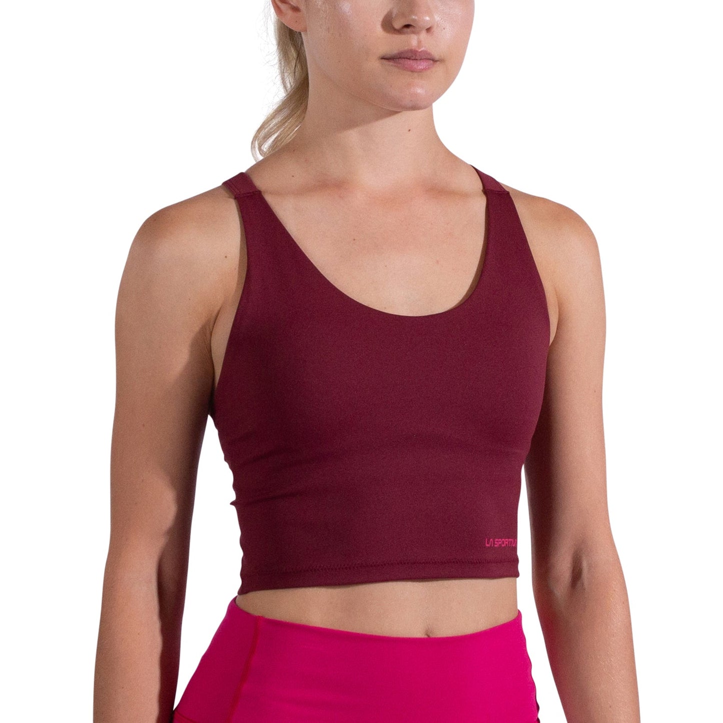 A woman wears the La Sportiva Cosmosis Bra Tank Women's, a sleeveless maroon top, paired with bright pink leggings, shown from shoulders to waist against a white background.