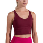 A woman wears the La Sportiva Cosmosis Bra Tank Women's, a sleeveless maroon top, paired with bright pink leggings, shown from shoulders to waist against a white background.