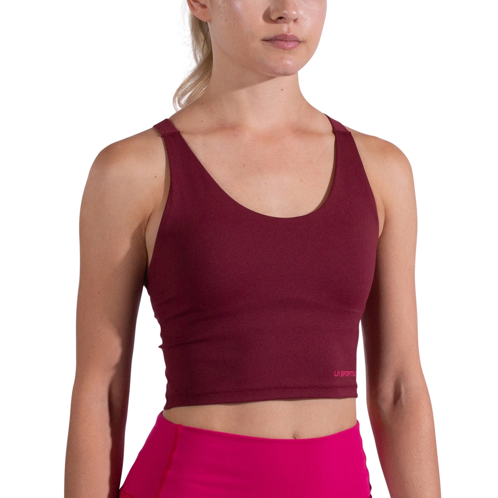 A woman wears the La Sportiva Cosmosis Bra Tank Women's, a sleeveless maroon top, paired with bright pink leggings, shown from shoulders to waist against a white background.