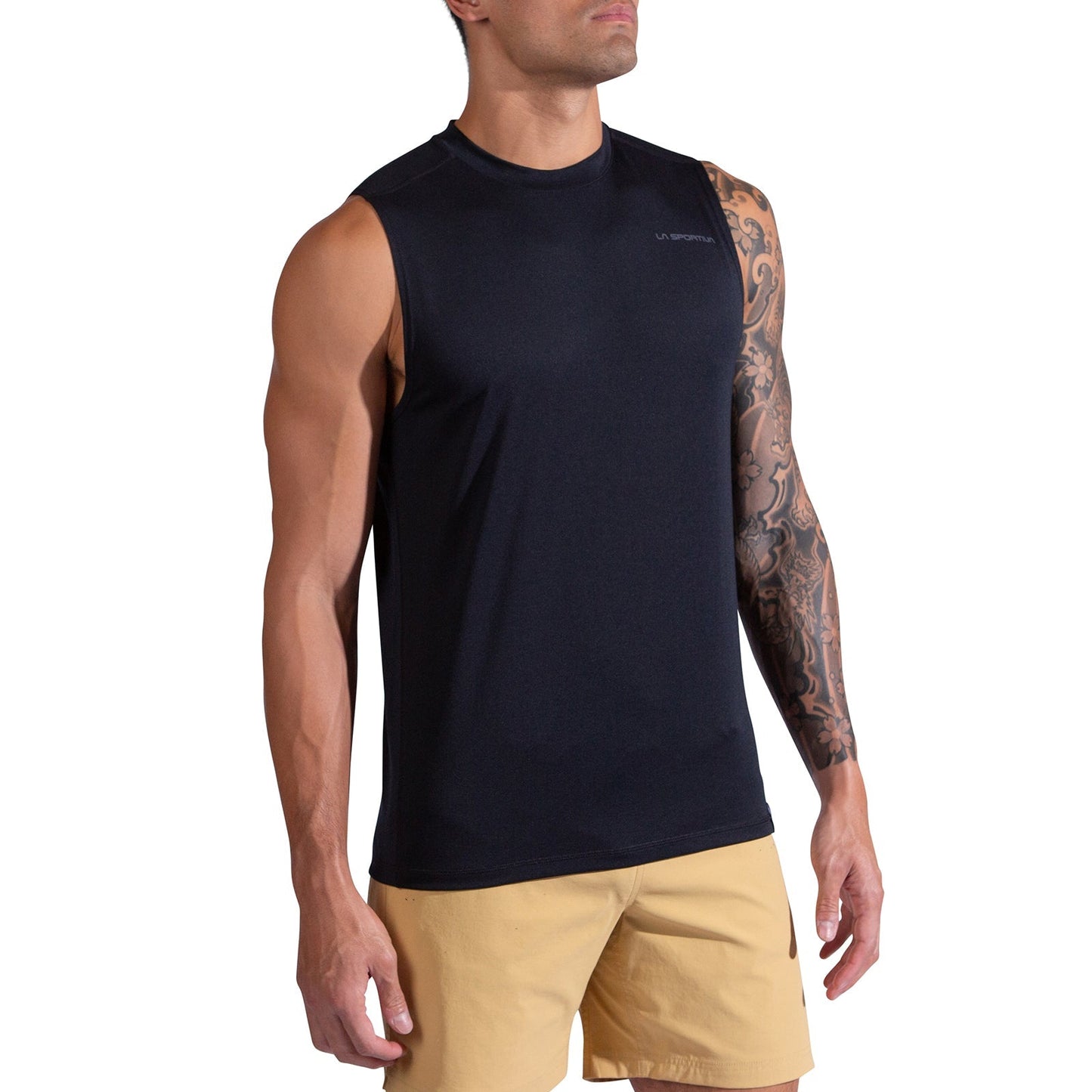 A man with a tattoo sleeve on his left arm stands facing slightly to the side in a La Sportiva Just Right Tank Men's in black and beige shorts against a white background.