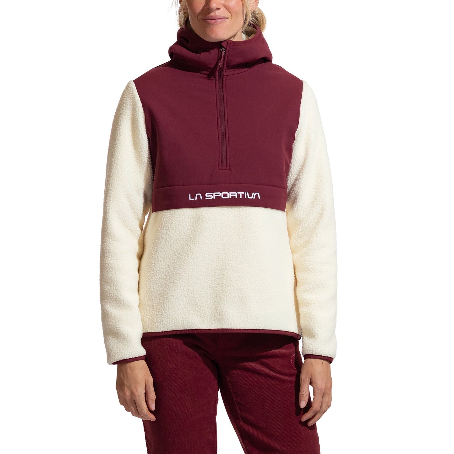 A woman wears the La Sportiva Guidance Sherpa Hoody in cream and burgundy, featuring long sleeves and "La Sportiva" on the front, styled as a cozy climbing jacket with matching burgundy pants.