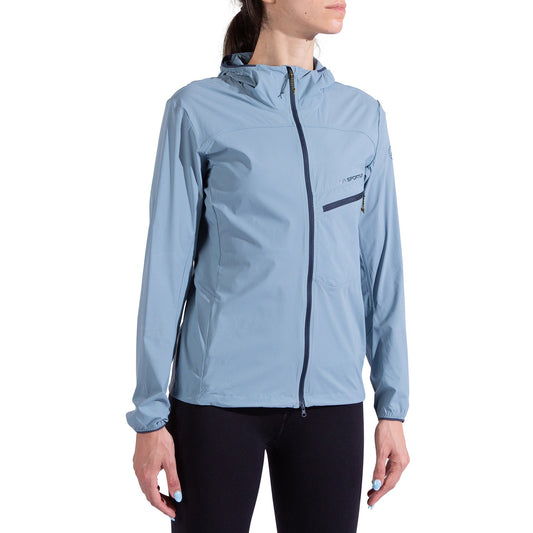 A woman in the La Sportiva Freeway Wind Jacket Women's in light blue with a chest pocket and black leggings stands against a white background.