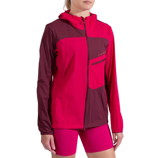 A woman in a La Sportiva Freeway Wind Jacket Women's, colored red and dark maroon, paired with matching red shorts, stands against a white background.