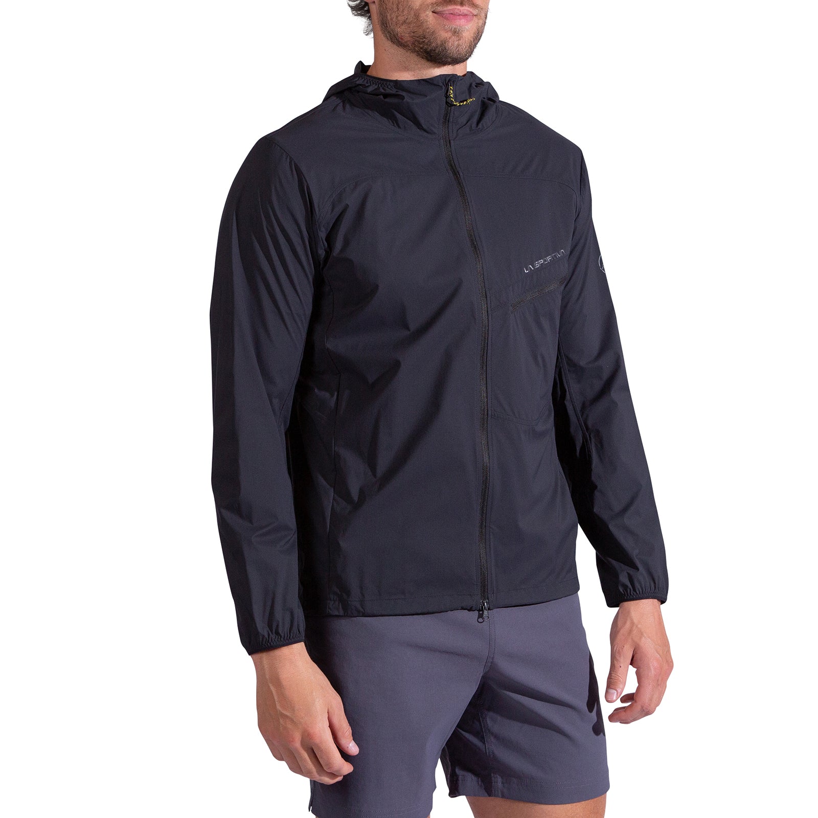 A man wearing the La Sportiva Freeway Wind Jacket Men's—an abrasion-resistant, ultralight jacket with a front zipper and elastic cuffs—paired with dark gray shorts, stands against a plain white background.