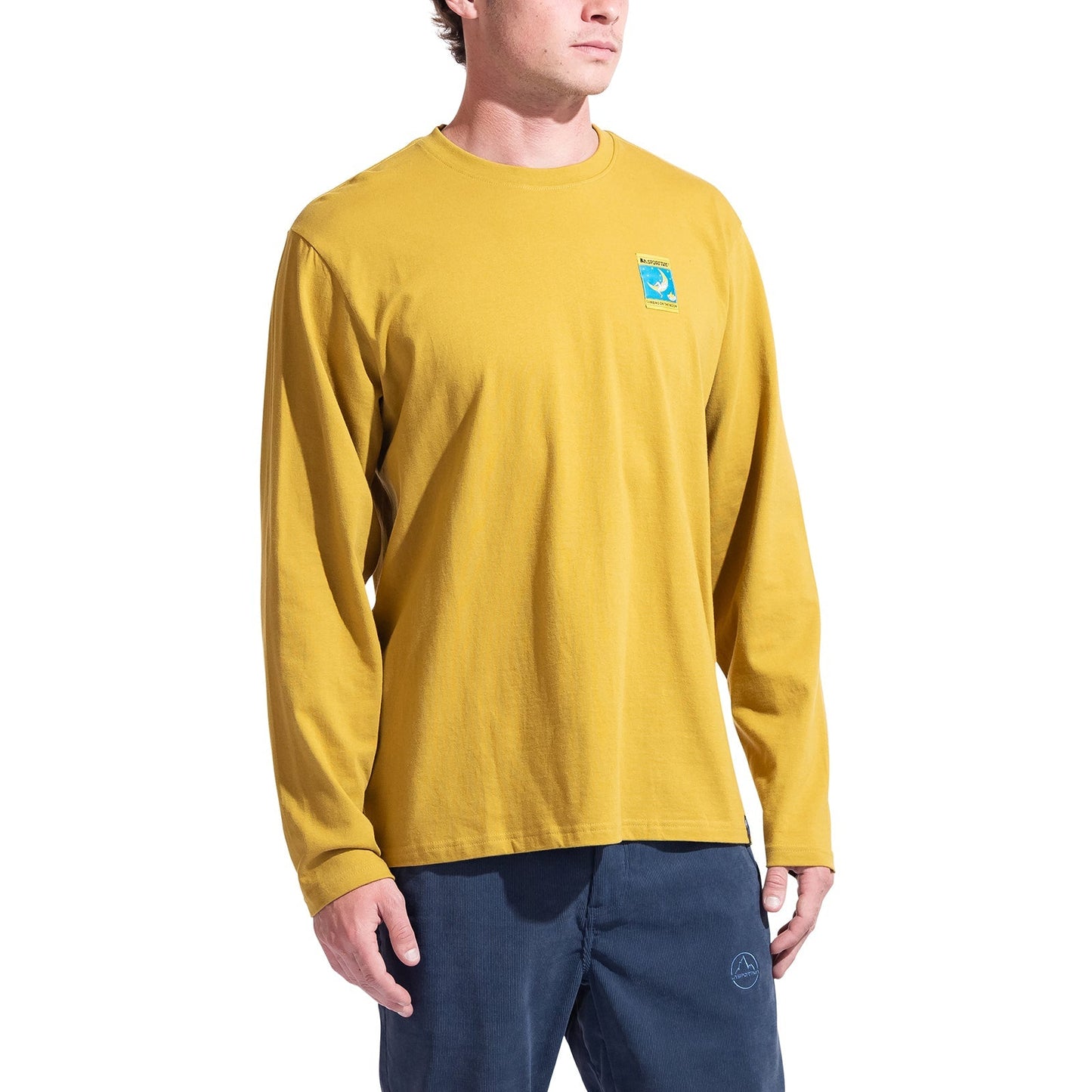 A person wearing the La Sportiva Moon Climb Long Sleeve Men's shirt in mustard yellow with a blue-green chest patch and dark blue pants stands against a white background—ideal for those inspired by climbing on the Moon.