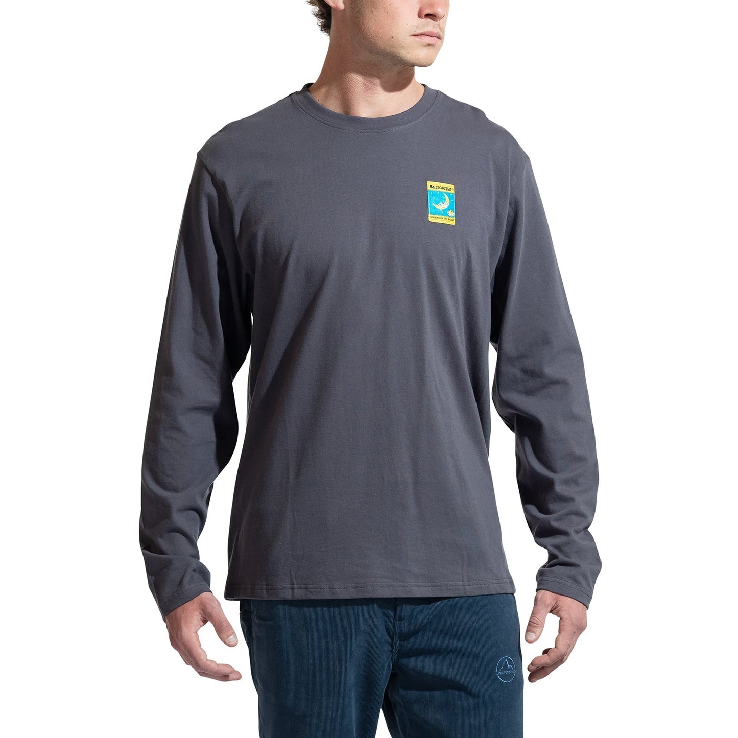 A man wears the La Sportiva Moon Climb Long Sleeve Men's shirt, an organic cotton dark gray climbing top with a small colorful left-chest graphic, standing against a plain white background.
