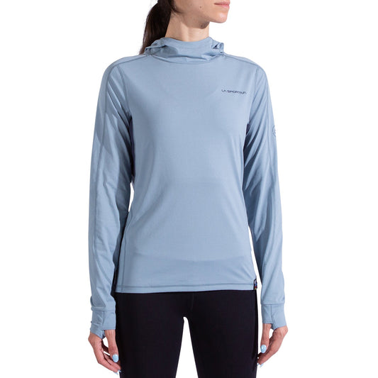 A woman wears the La Sportiva Cloud Shadow Sun Hoody—a lightweight, light blue UPF 50 long-sleeve with thumb holes—paired with black leggings, standing against a white background.