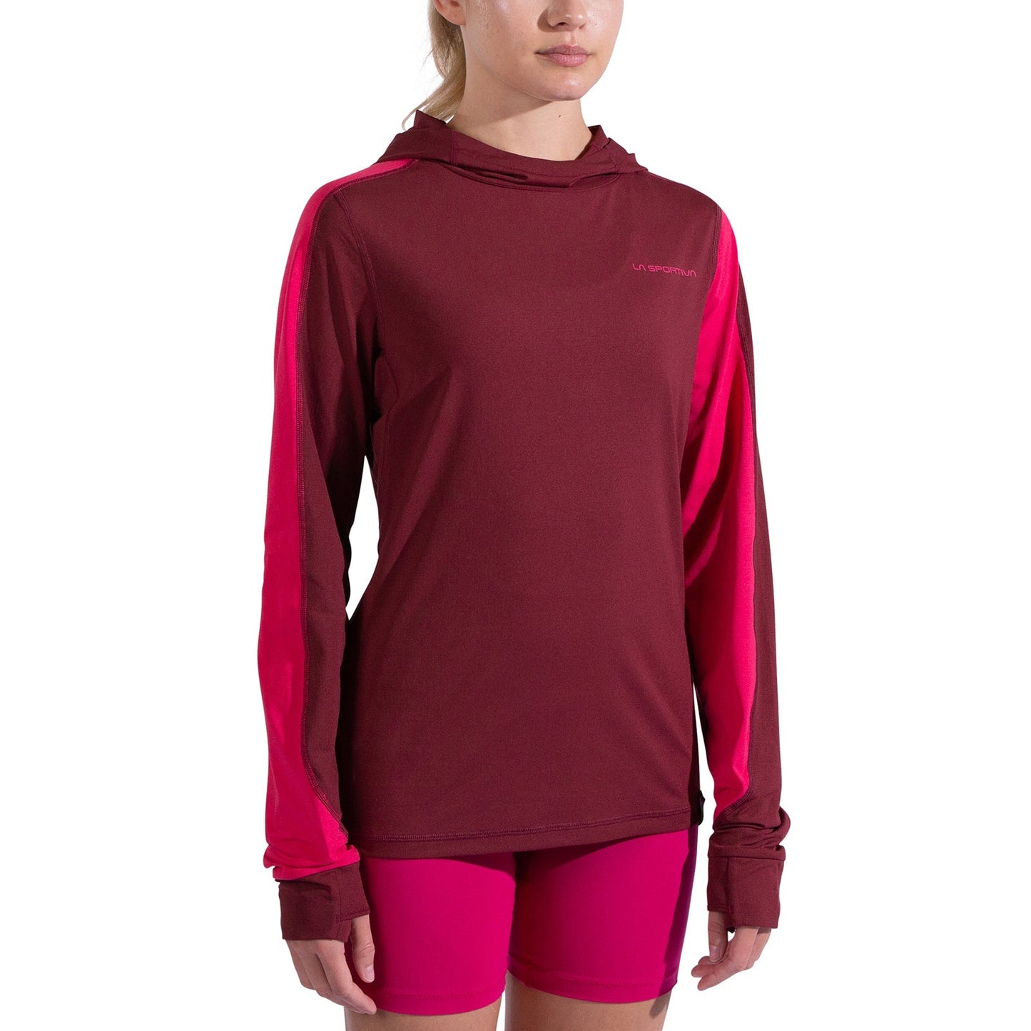 A woman wearing the La Sportiva Cloud Shadow Sun Hoody Women's in maroon with bright pink accents and matching pink shorts stands against a white background. The hoody offers UPF 50 protection, perfect for outdoor activities.