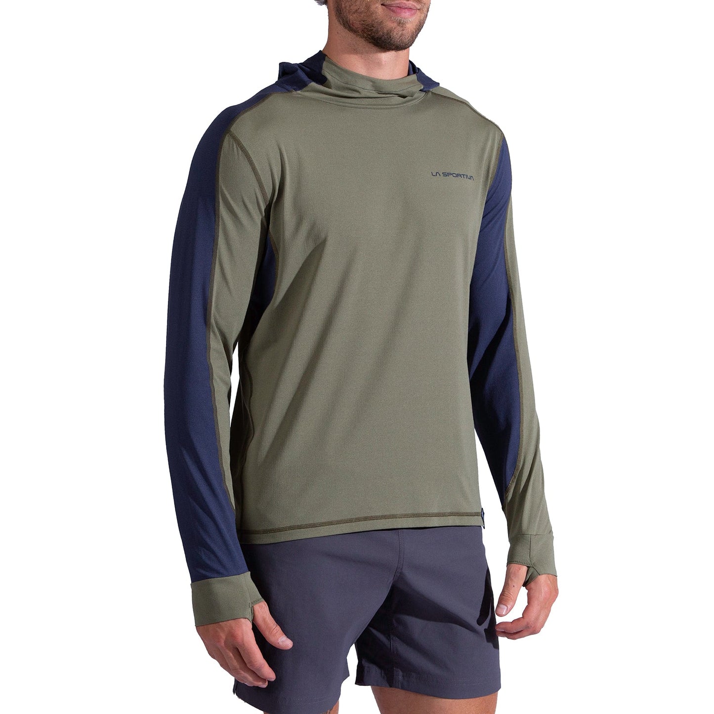 A man wears the La Sportiva Cloud Shadow Sun Hoody Men's, a lightweight olive green and navy long-sleeve with thumbholes, paired with dark shorts, standing against a plain white background.