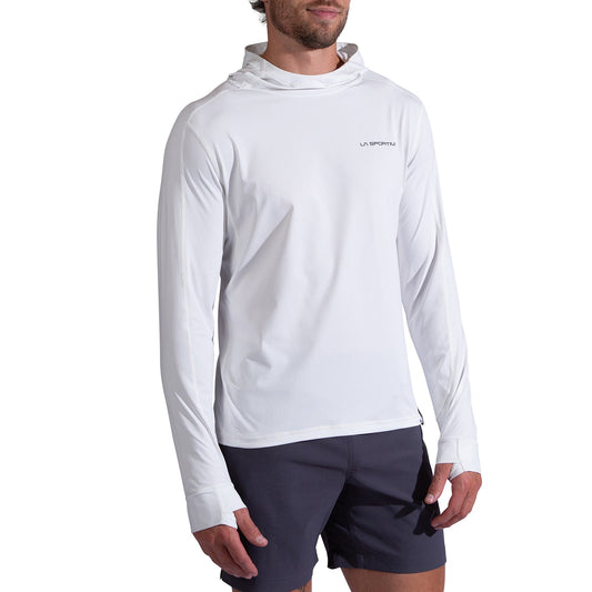 A man wearing the La Sportiva Cloud Shadow Sun Hoody Men's in white with thumbholes and black shorts stands against a white background. The hoody features a chest logo and provides UPF 50+ sun protection.