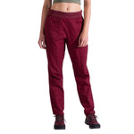 A person wearing a green crop top and La Sportiva Roots Pants Women's in burgundy, featuring an elastic waistband, articulated knees, and pockets, stands with arms relaxed by their sides. They are also wearing dark hiking shoes.