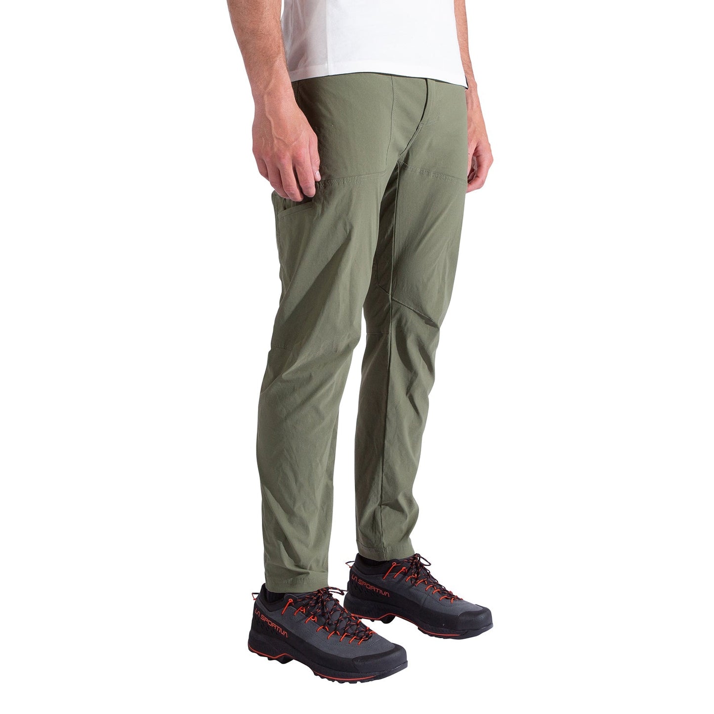 A person wearing La Sportiva Talus Pants Men’s in olive green, paired with a white shirt and black hiking shoes with red laces, stands against a plain white background.