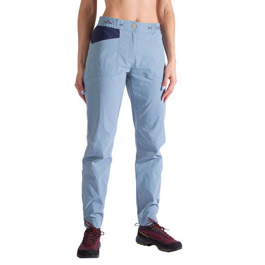 A woman wears La Sportiva Mantra Pants in light blue, featuring a navy pocket detail, paired with black and red hiking shoes, standing against a white background. The image displays the pants from waist to feet.
