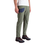 A man wears La Sportiva Labyrinth Pants Men's in olive green with an adjustable waistband and blue pocket, paired with a white shirt and black hiking boots with red laces, standing against a white background.