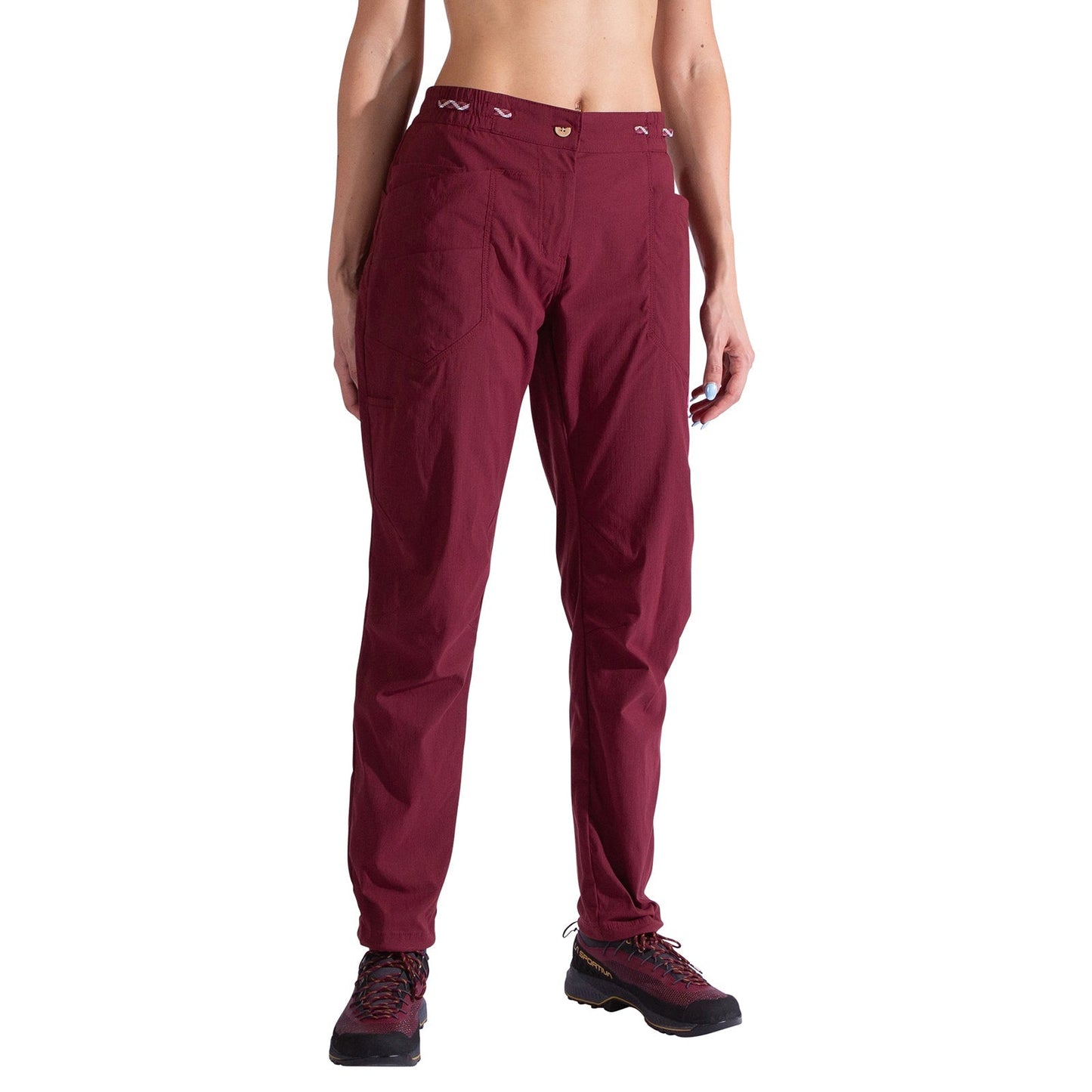 A person wears La Sportiva Labyrinth Pants Women's in burgundy, made from durable fabric, and black hiking shoes. Only their lower torso and legs are visible against a white background.