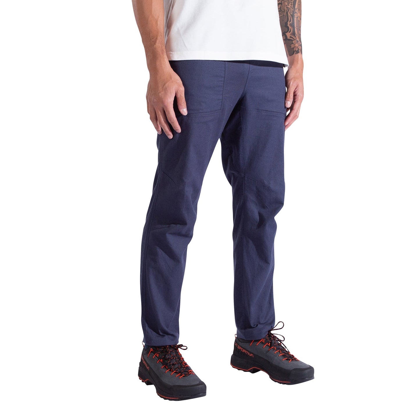 Only the lower half of a person is visible as they stand against a white background, wearing La Sportiva Bolt Pants Men's in navy blue and black hiking shoes with orange laces.