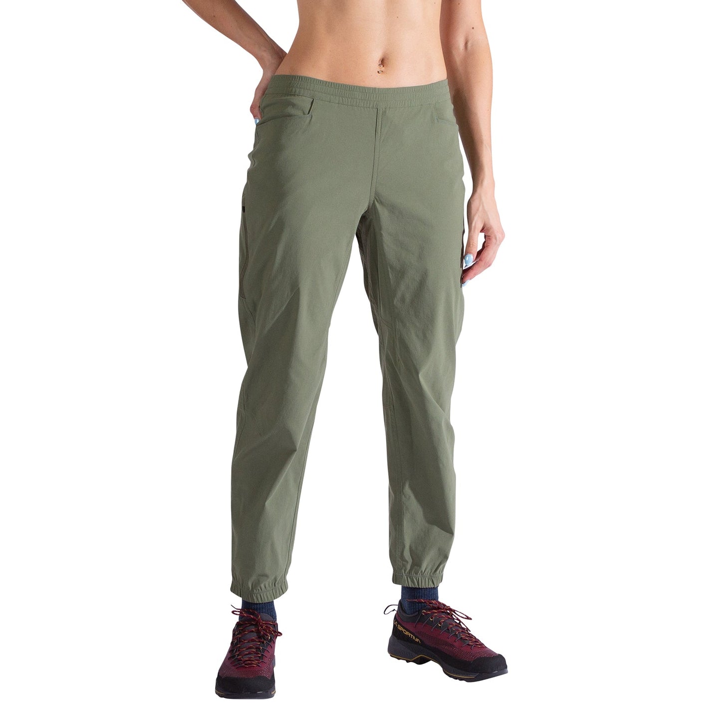 A person models the La Sportiva Gambit Pants Women's in olive green with maroon hiking shoes, posing against a white background—one arm bent, the other relaxed.
