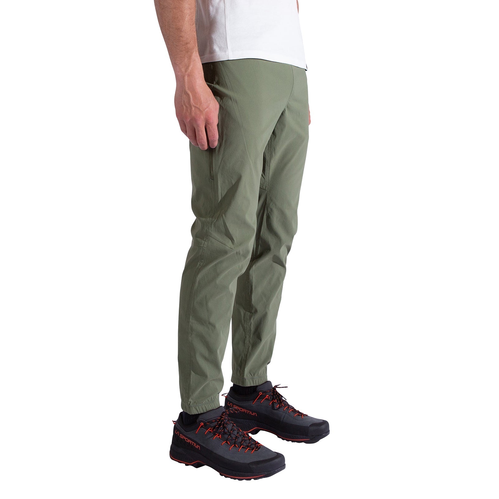 A person wearing La Sportiva Gambit Pants Men's in olive green, a white t-shirt, and black hiking shoes with red laces stands against a white background; only the lower half of the body is visible.