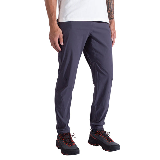 A person is wearing La Sportiva Gambit Pants Men's in dark gray, paired with a white shirt and black hiking shoes with red laces, standing against a white background.