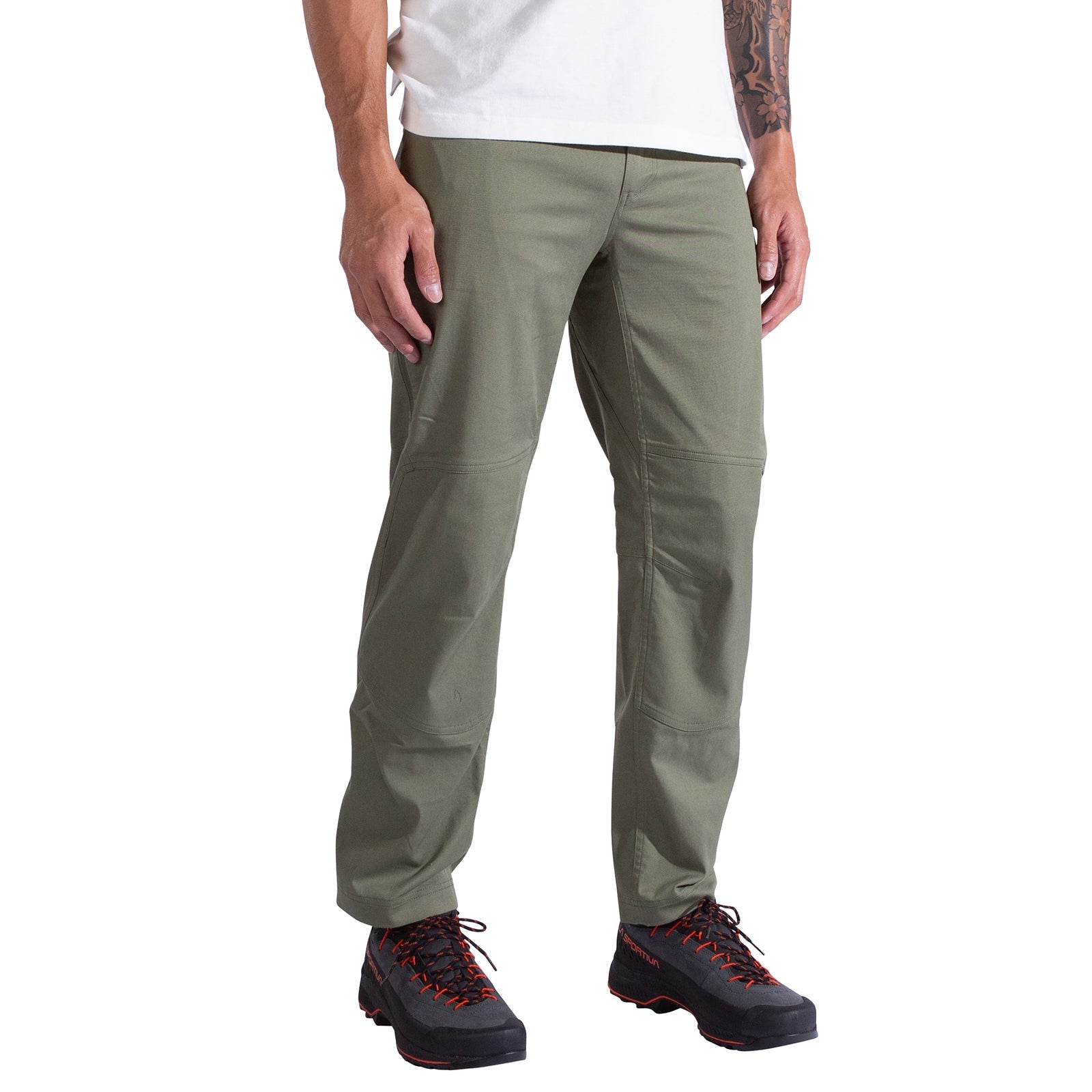 A person wearing La Sportiva Mainliner Pants Men's in olive green, a white t-shirt, and black hiking shoes with orange laces stands against a white background.