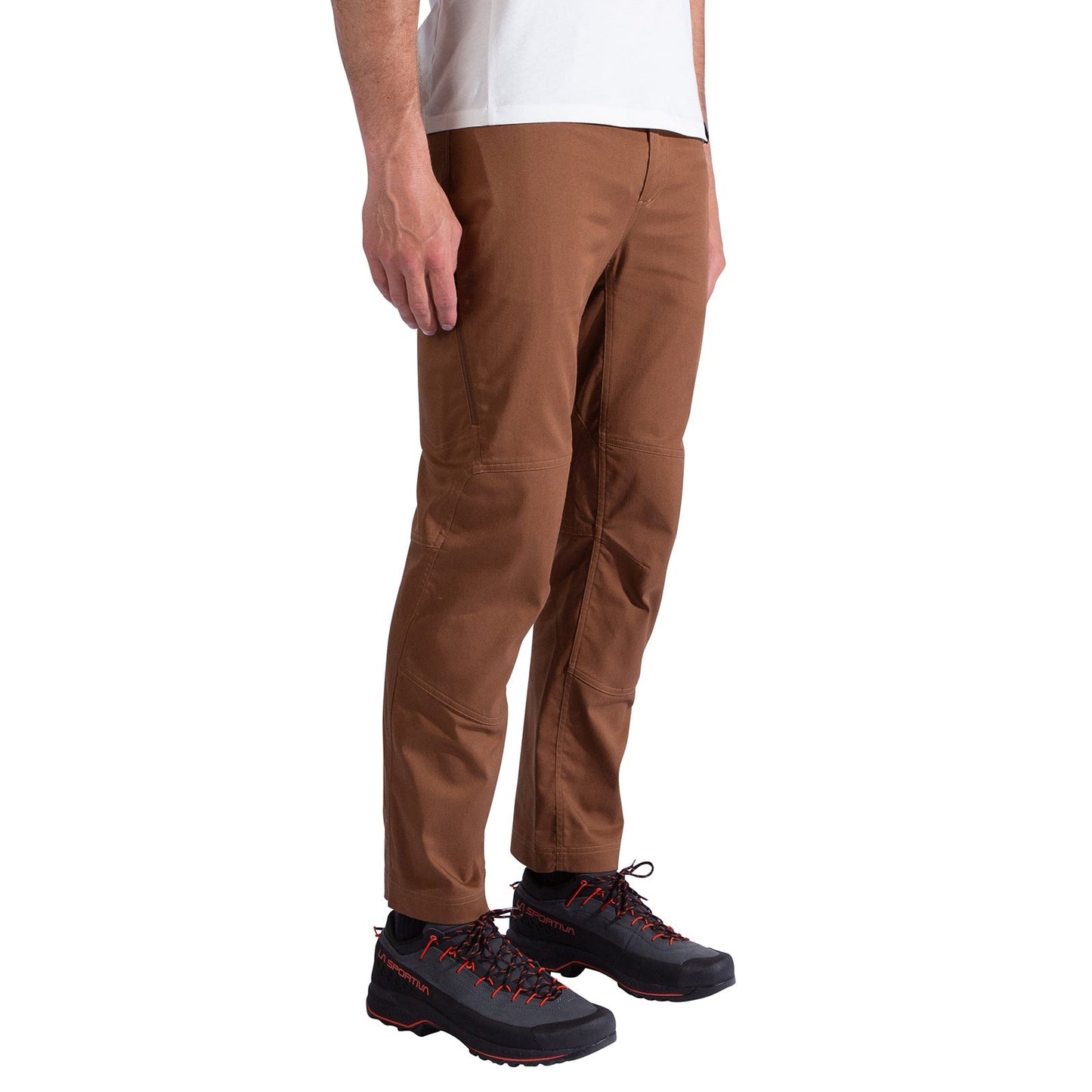 A person stands sideways, showing the fit and style of La Sportiva Mainliner Pants Men's in brown organic cotton, paired with a white shirt and black hiking shoes with red laces.