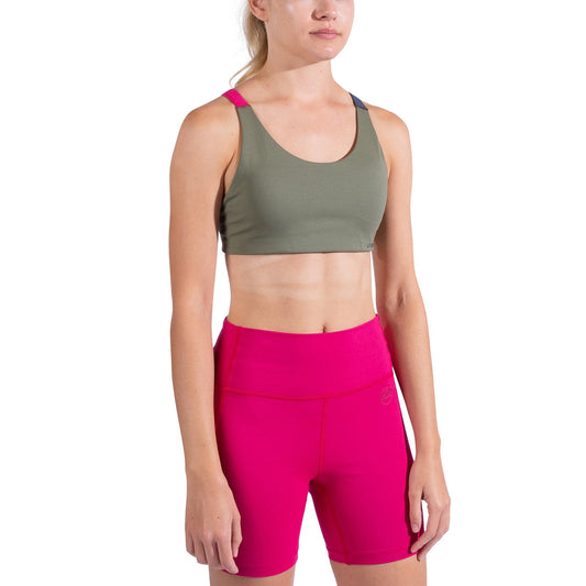A woman stands against a white background wearing the La Sportiva Cosmosis Bra Women's in green and bright pink high-waisted shorts, showcasing breathable, supportive activewear ideal for any workout.