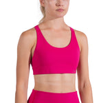 A woman wears the La Sportiva Cosmosis Bra Women's in bright pink, paired with matching high-waisted leggings, standing against a white background. Her hair is tied back and only part of her face is visible in the frame.