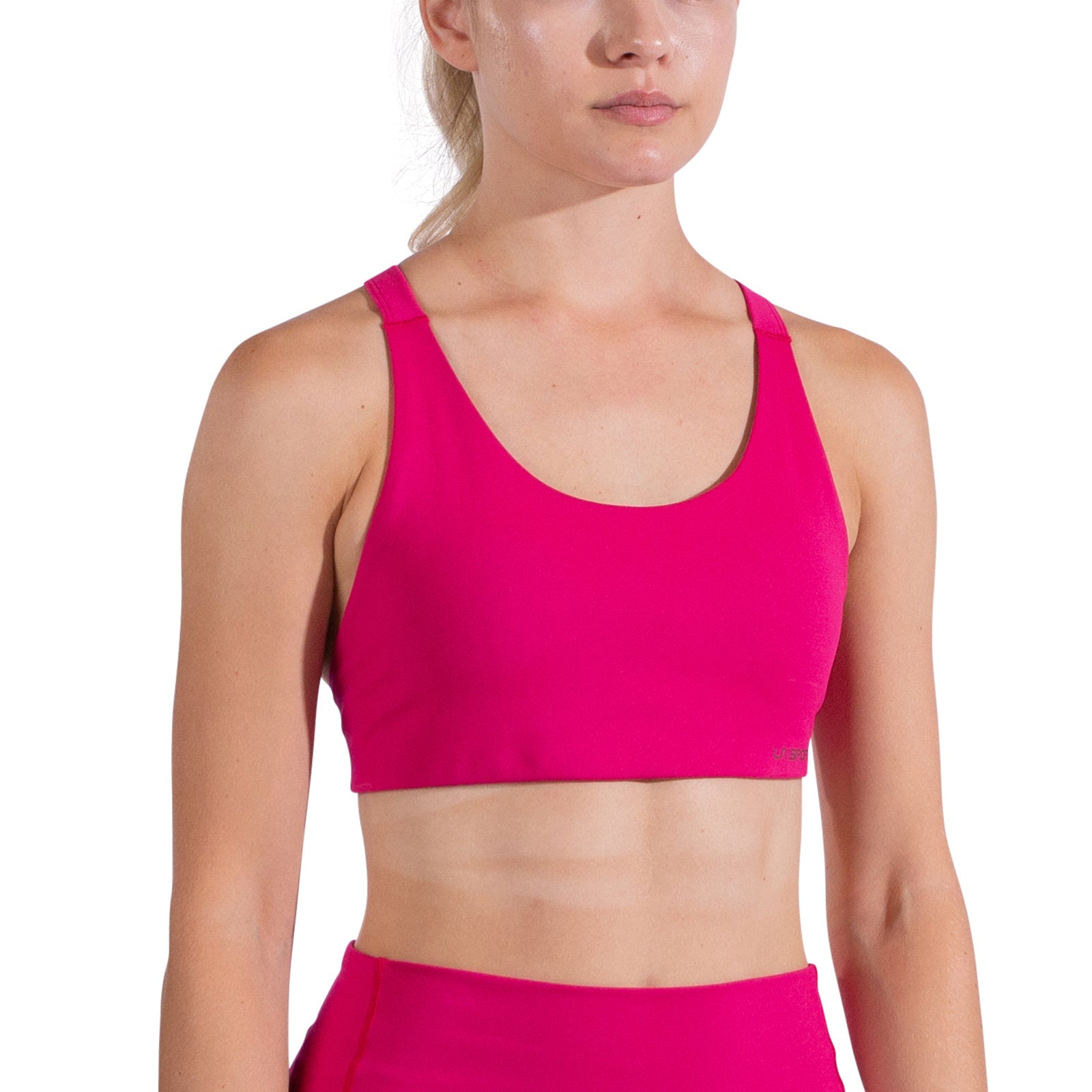 A woman wears the La Sportiva Cosmosis Bra Women's in bright pink, paired with matching high-waisted leggings, standing against a white background. Her hair is tied back and only part of her face is visible in the frame.