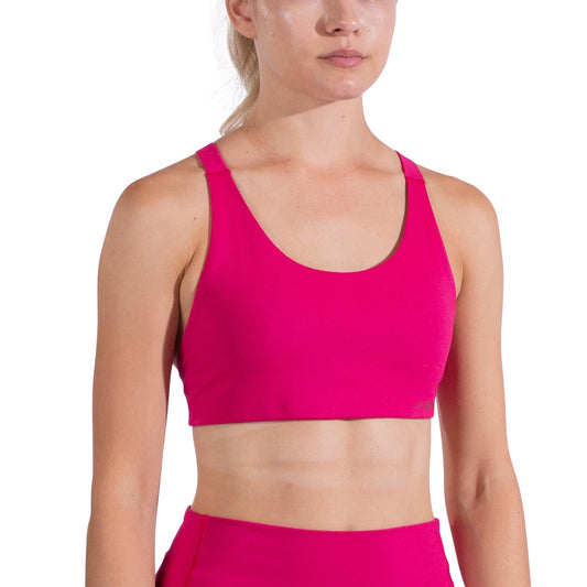 A woman wears the La Sportiva Cosmosis Bra Women's in bright pink, paired with matching high-waisted leggings, standing against a white background. Her hair is tied back and only part of her face is visible in the frame.