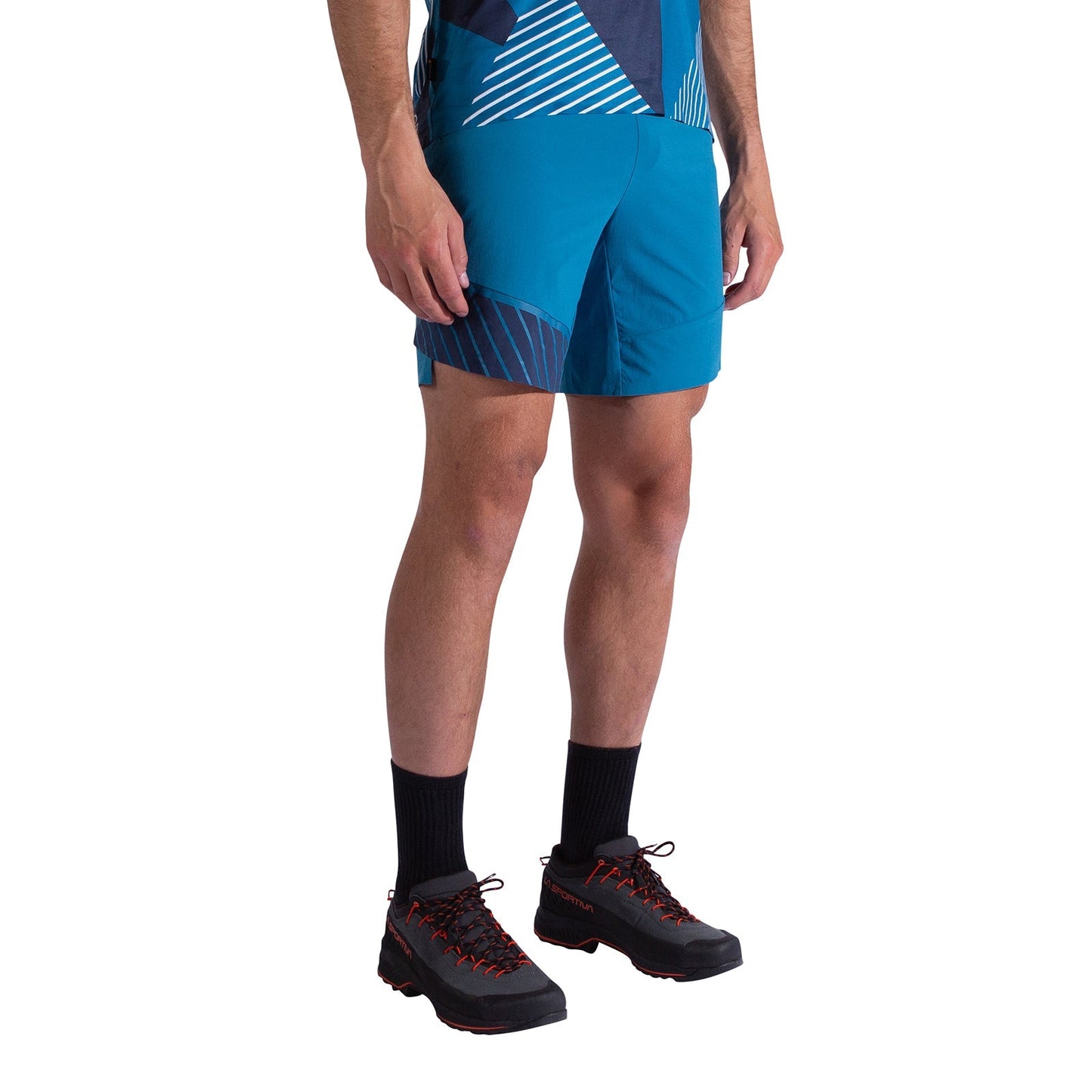 A person wearing La Sportiva Comp Shorts Men's and a blue patterned shirt, along with black socks and black hiking shoes with red laces, stands against a white background. Their upper body is partially out of frame.