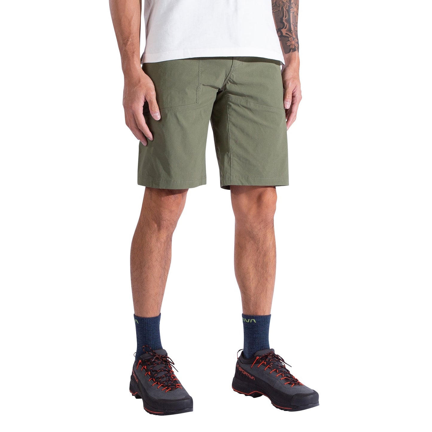A person is shown from the waist down wearing La Sportiva Talus Shorts Men's in olive green, paired with a white T-shirt, navy socks, and black hiking shoes. The relaxed pose highlights the shorts' recycled fabric design.