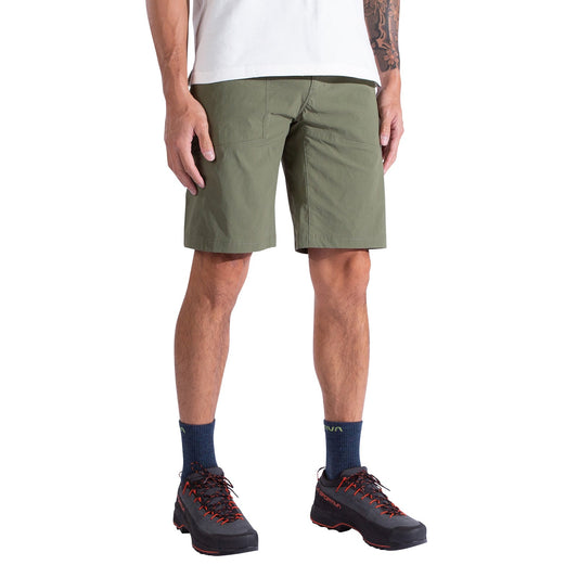 A person is shown from the waist down wearing La Sportiva Talus Shorts Men's in olive green, paired with a white T-shirt, navy socks, and black hiking shoes. The relaxed pose highlights the shorts' recycled fabric design.