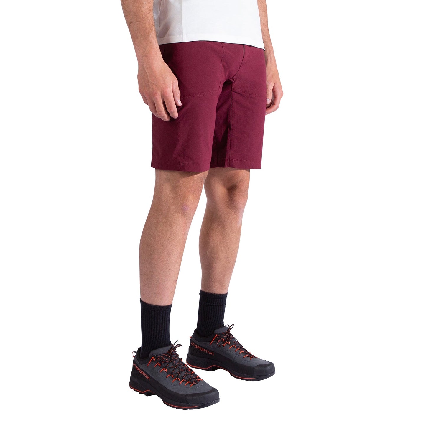 A person wearing a white shirt, La Sportiva Talus Shorts Men's in burgundy, black socks, and black trail shoes with red accents stands against a plain white background.