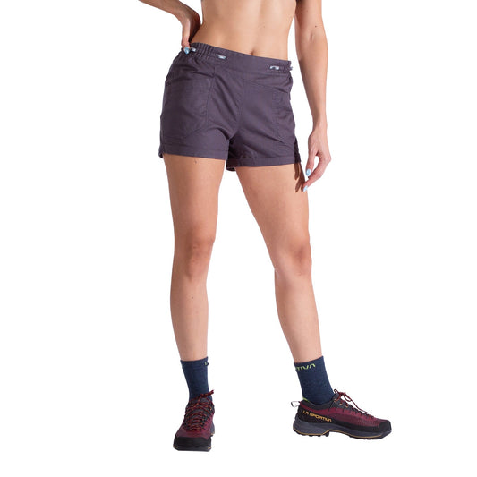 A person stands against a white background wearing La Sportiva Bolt Shorts Women's in dark gray with an adjustable waistband, black socks, and burgundy trail shoes. Their torso is partially visible, one arm on their hip, the other relaxed.