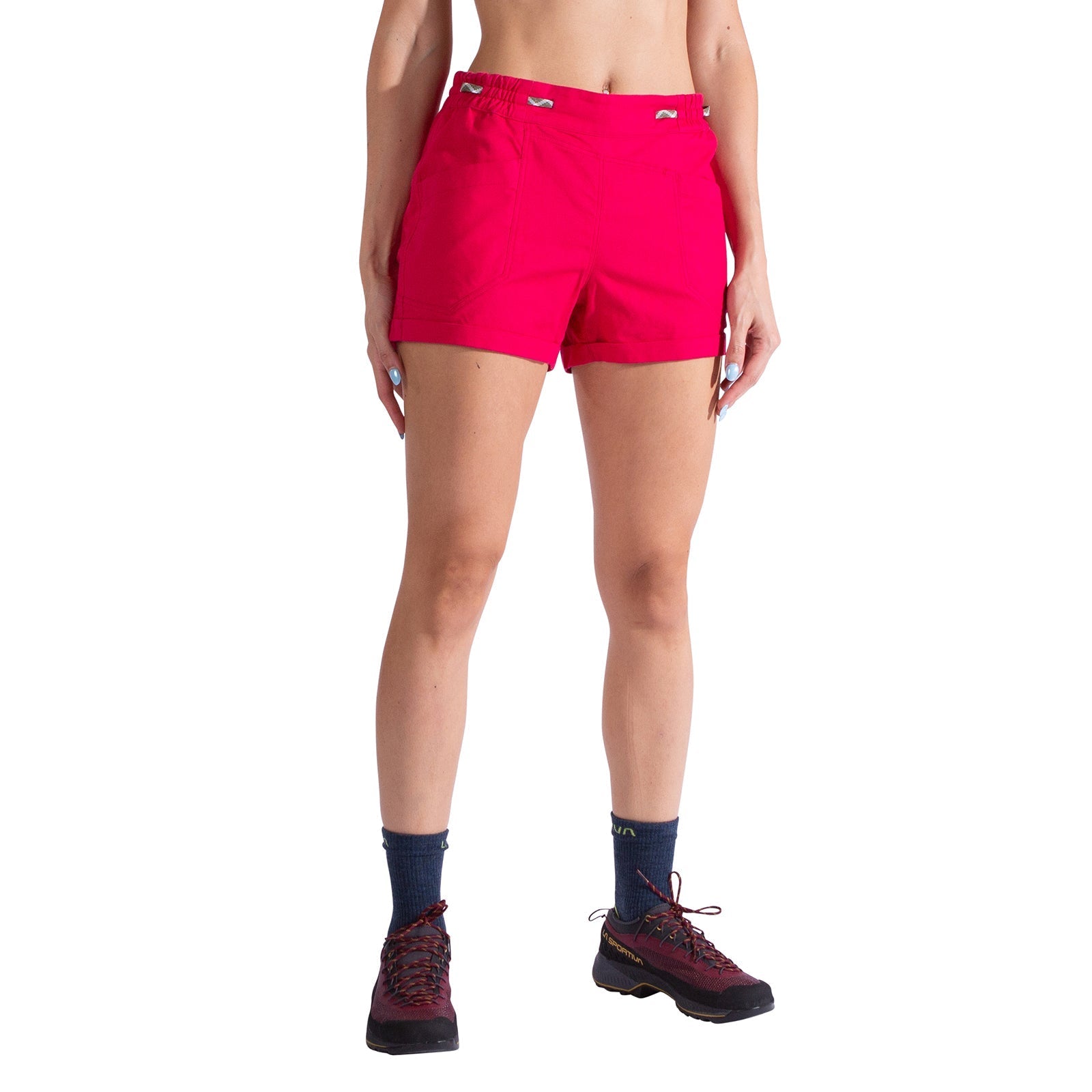 A person models the La Sportiva Bolt Shorts Women's in bright pink, featuring an adjustable waistband. They pair the shorts with navy socks and black hiking shoes, standing against a plain white background with their upper body cropped out.
