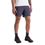A person wears a white shirt, La Sportiva Gambit Shorts Men's in dark navy, navy socks, and black trail shoes with red laces, shown from shoulders to feet against a white background.