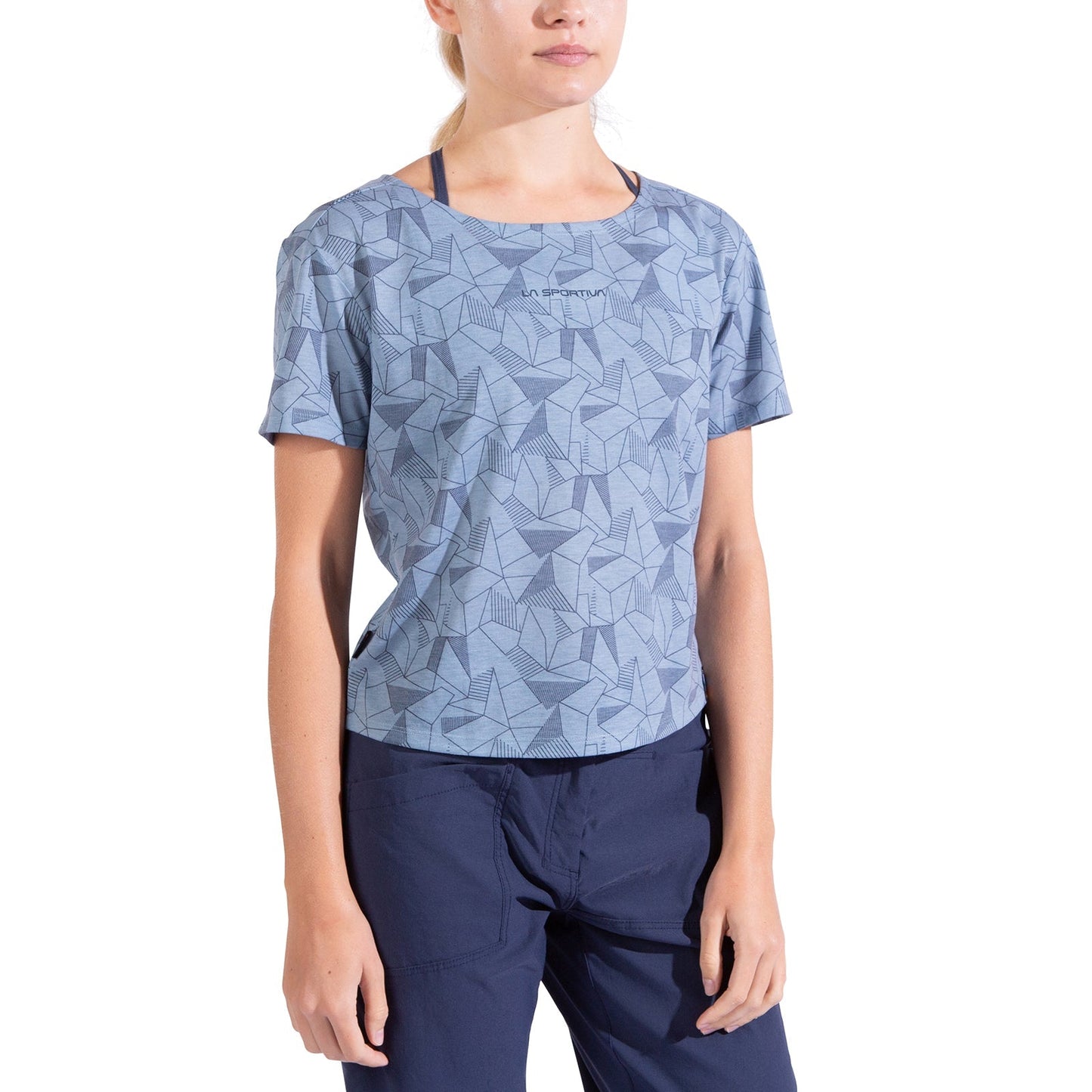A woman wears the La Sportiva Dimension T-Shirt Women's in light blue with a geometric pattern and baggy fit, paired with dark blue pants. She stands with relaxed arms, her face partially out of frame.