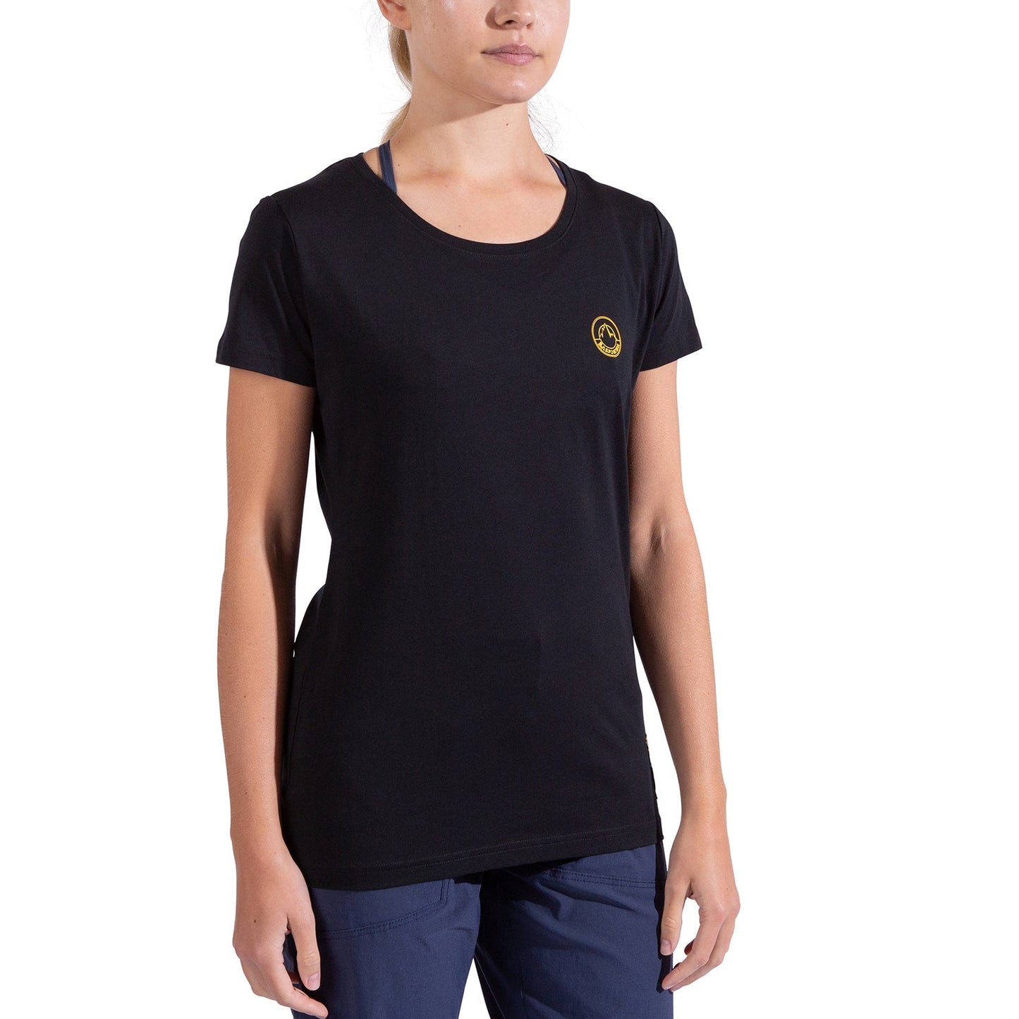 A woman wears the La Sportiva Climbing on the Moon T-Shirt Women's—plain black with a small yellow logo—paired with navy blue pants, standing against a white background. Her face is partially out of frame.