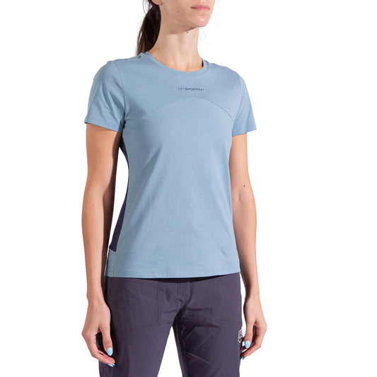 A woman wears the La Sportiva Roof T-Shirt Women's in light blue with short sleeves and dark pants, standing with arms relaxed at her sides against a plain white background.