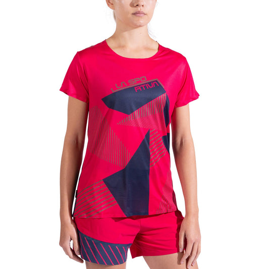 A woman stands against a white background wearing La Sportiva's Comp T-Shirt Women's in bright pink with a graphic navy and red pattern, paired with matching shorts.
