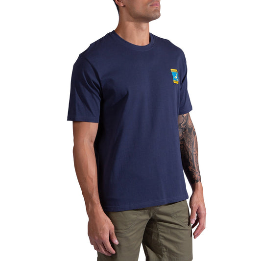 A man wears the La Sportiva Moon Patch T-Shirt Men's in navy blue (organic cotton, small colorful chest graphic) with olive green pants against a white background—a perfect casual look for climbers.