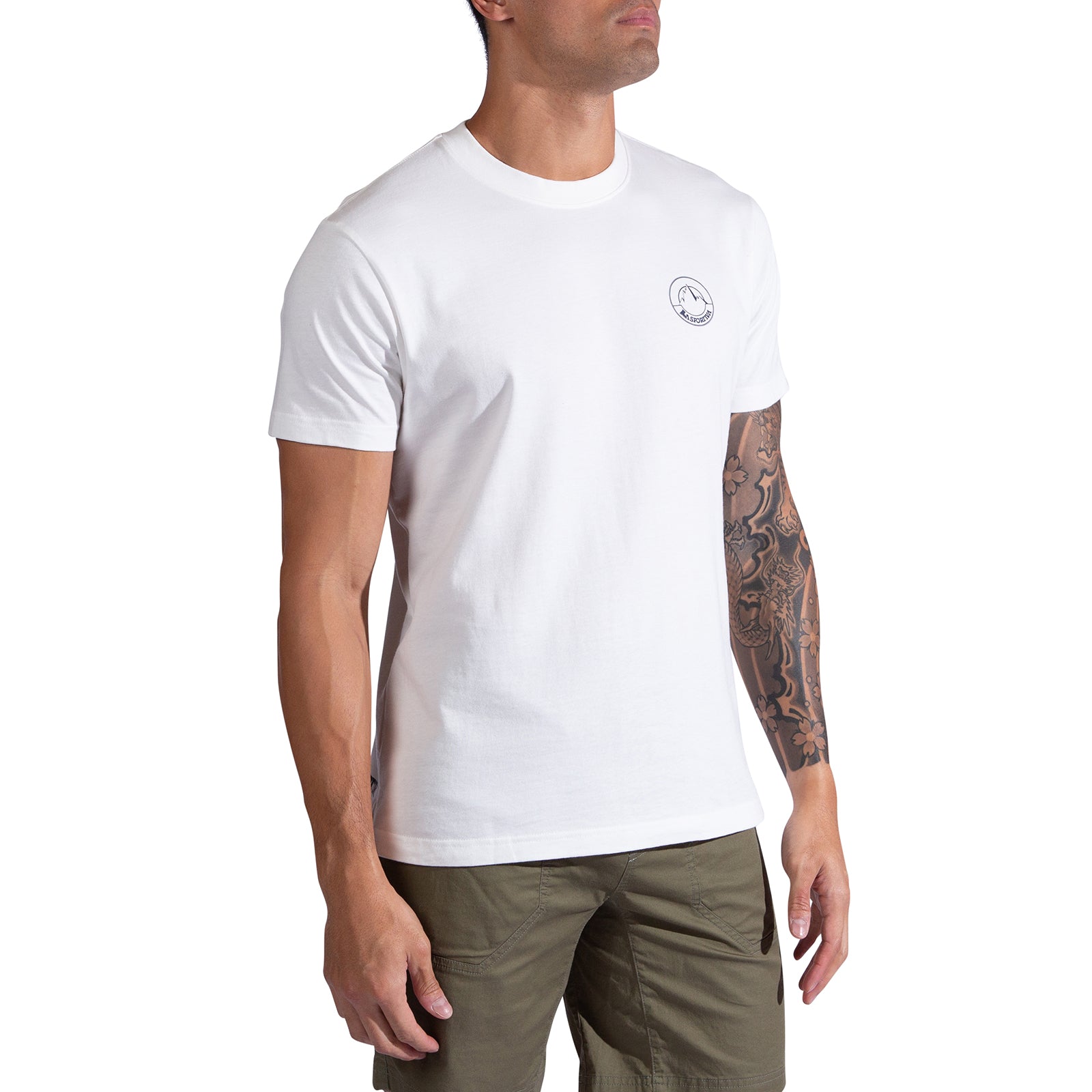 A man stands against a white background wearing the La Sportiva Circle Logo T-Shirt Men's in plain white, featuring a small circular logo on the chest, paired with olive green shorts. His right arm displays a detailed tattoo sleeve.