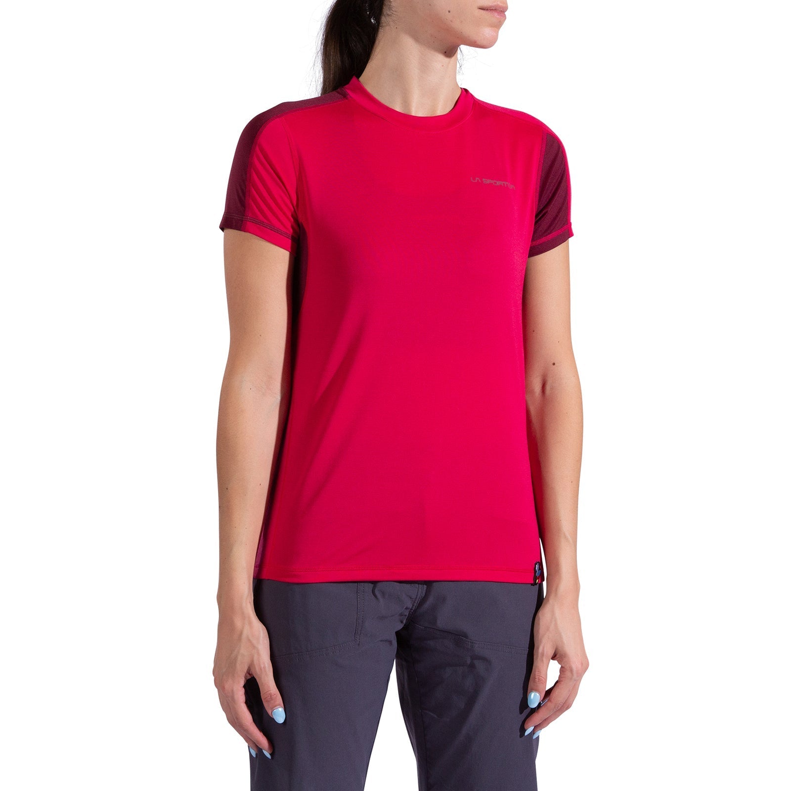 A woman wears the La Sportiva Just Right T-Shirt Women's in bright pink with dark red sleeves and dark pants, standing with her arms relaxed by her sides against a plain white background.