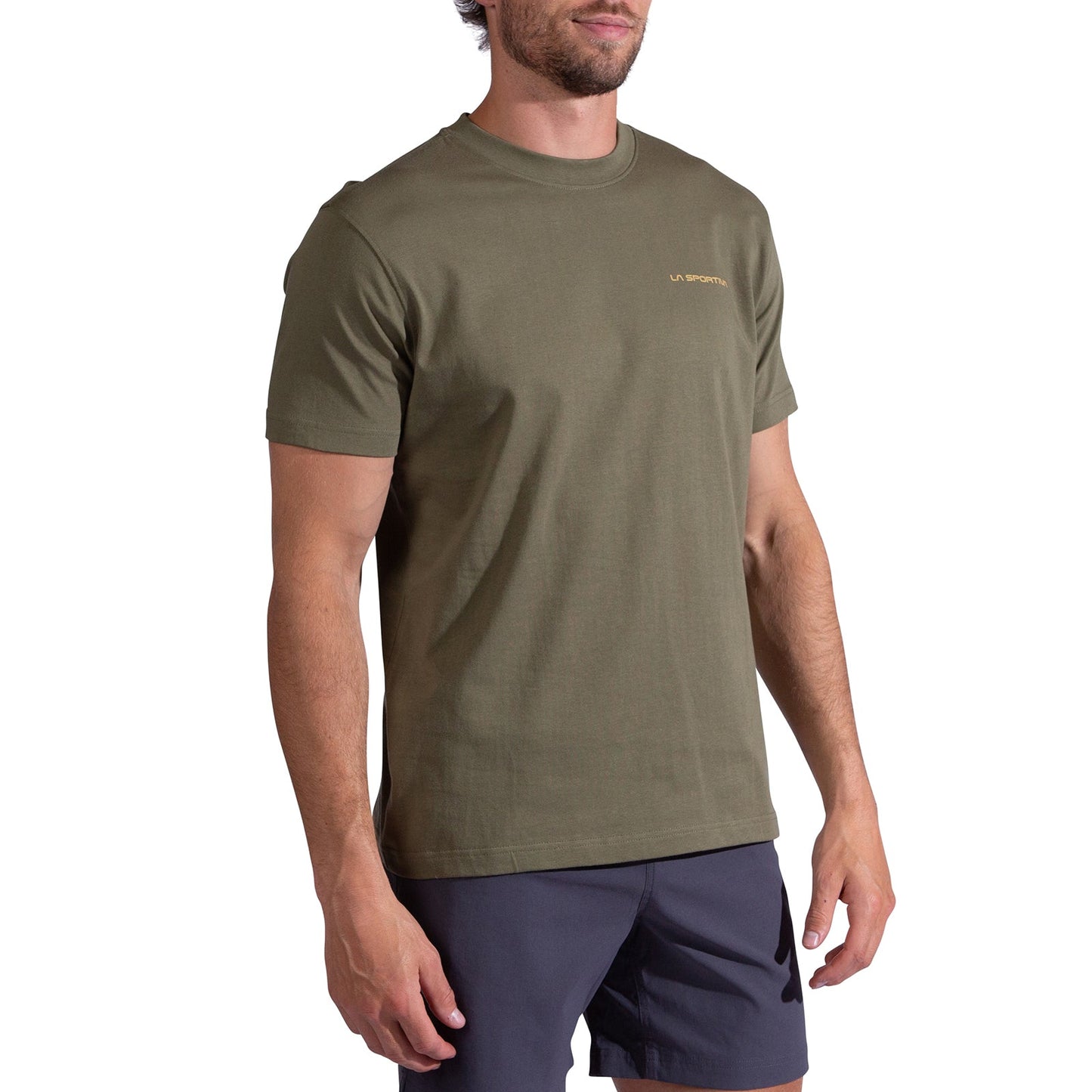 A man wearing a La Sportiva Trilogy T-Shirt Men's in olive green with short sleeves and a small chest logo, paired with dark shorts, stands against a plain white background.